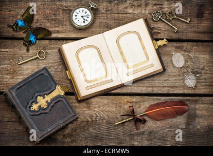 Libri antichi, la scrittura di accessori e butterfly su legno rustico sfondo. tasti vintage, orologio da tasca, bicchieri e piuma Foto Stock