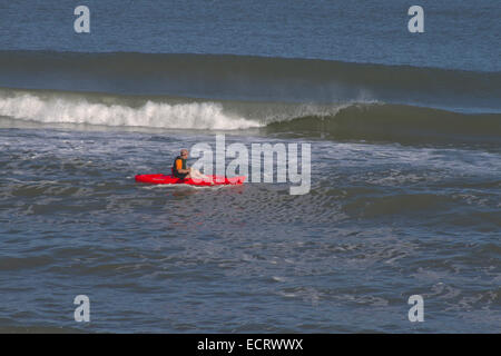 Un uomo in un rosso brillante e kayak giallo oar pale da un grande e la rottura delle onde oceaniche Foto Stock