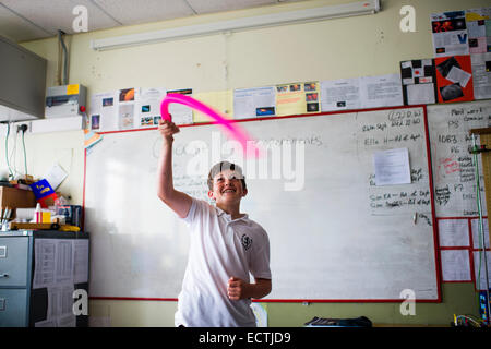 Secondary School Science Education Wales UK: un ragazzo di suoni e note musicali agitando un tubo incavate sopra la sua testa in una classe fisica lezione esperimento Foto Stock