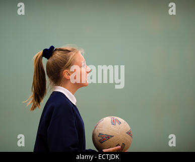 Scuola secondaria educazione fisica Wales UK: una ragazza adolescente in profilo a giocare una palla di gioco netball basket tenendo una palla in palestra, i suoi capelli in una coda di cavallo Foto Stock