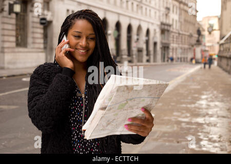 Giovane donna al telefono tenendo una mappa Foto Stock