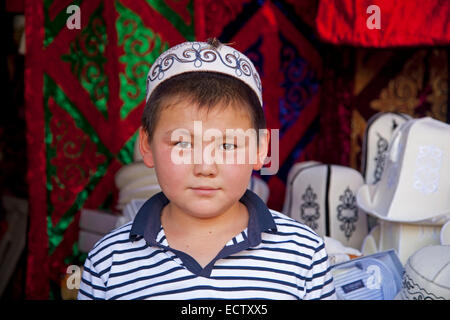 Ragazzo del Kirghizistan indossando il tradizionale tubeteika al mercato in materia di SSL, Kirghizistan Foto Stock
