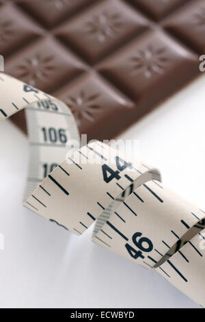 Una misura di nastro con una defocussed barra di cioccolato nel retro di massa. Il simbolo di diete e di tentazione. Foto Stock