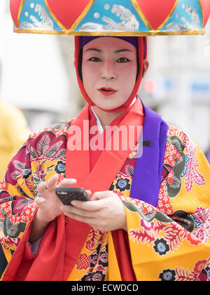 La donna nel tradizionale danza ryukyu costume con Hanagasa hat utilizzando iPhone. Il Castello di Shuri Festival tenutosi nella città di Naha, Okinawa. Foto Stock