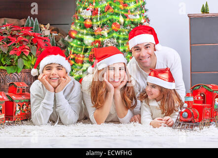 Allegro genitori con due simpatici ragazzi sorridenti sdraiati vicino a albero di Natale a casa per celebrare il Natale, festa della scheda Messaggi di saluto Foto Stock