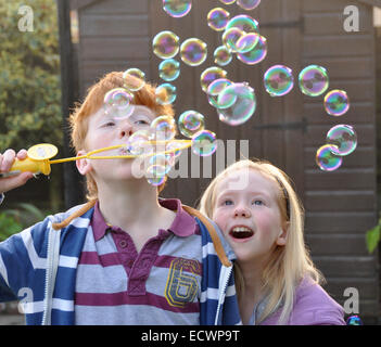 I bambini a soffiare bolle; zenzero pelose ragazzo con giovane sorella Foto Stock