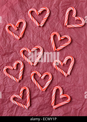 Tettuccio di colpo di mini candy canes formare forme di cuore su una carta velina rossa sullo sfondo. Formato verticale. Foto Stock