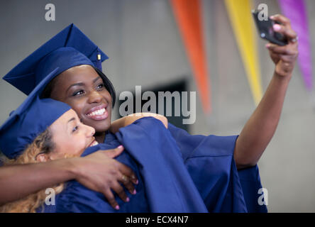 Due sorridenti studentesse tenendo selfie a graduazione Foto Stock