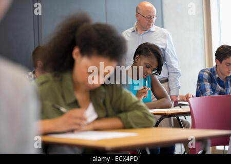 Insegnante camminando lungo la scrivania e controllare gli studenti durante il test Foto Stock