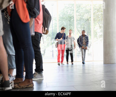 Tre studenti di sesso maschile a camminare lungo il corridoio a parlare con grande finestra in background Foto Stock