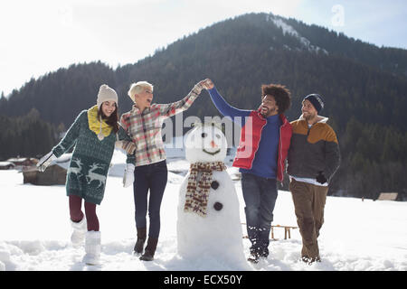 Amici a giocare intorno pupazzo di neve Foto Stock