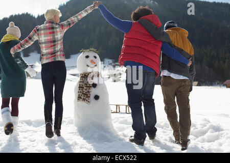 Amici a giocare intorno pupazzo di neve Foto Stock