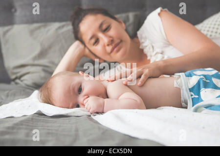 Ritratto di piccolo bambino succhiare il pollice con la madre sorridente in background Foto Stock