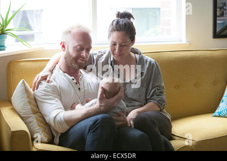I genitori sorridente e azienda piccolo bambino seduto sul divano giallo Foto Stock
