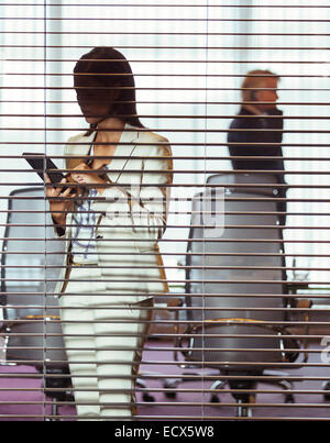 Imprenditrice utilizzando tablet pc in piedi in sala conferenze dietro persiane Foto Stock
