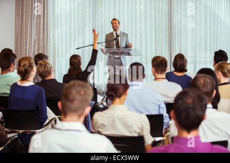 Imprenditore dando il discorso in sala conferenze, donna dal pubblico alzando la mano Foto Stock
