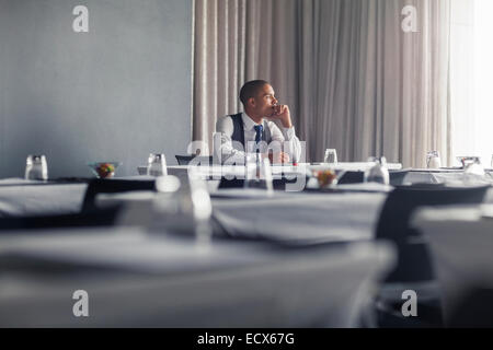 Ritratto di giovane uomo seduto a tavola in vuote sala conferenze guardando attraverso la finestra
