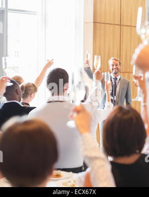 Ritratto di uomo sorridente davanti al pubblico in sala conferenze, sollevamento del pane tostato con flute da champagne Foto Stock