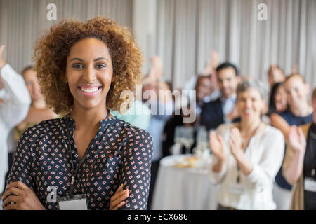 Ritratto di sorridente giovane donna in sala conferenze con la gente applaude in background Foto Stock
