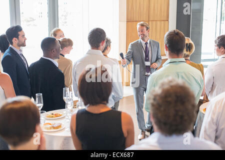 Ritratto di uomo sorridente in piedi nella sala conferenze, offrendo il microfono per persona in udienza Foto Stock