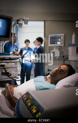 Paziente sdraiato a letto in unità di cura intensiva, dottori discutendo in background Foto Stock
