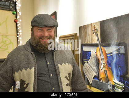 Huntington, New York, Stati Uniti d'America. Xx Dec, 2014. Un sorridente barbuto giovane uomo che indossa un maglione campestre con poggia su di essa considera un tema musicale della verniciatura di un violino e spartiti musicali, presso il jingle Boom Holiday Bash ha entertainment dotato di parola spettacoli e musica dal vivo, più finestre decorate da artisti e i premi per la gente che indossa il più creativo o brutto maglioni, presso la strada principale galleria di Huntington Arts Council. Sparkboom, un progetto HAC, fornisce eventi come questo orientata a gen-Y, 18-34 anni di età, per affrontare la fuga dei cervelli dei giovani creativi professionisti Foto Stock