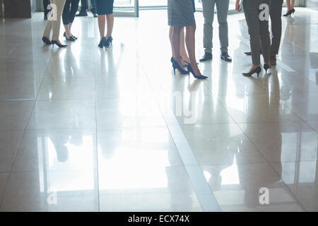 Sezione bassa della gente di affari in piedi nella hall, con riflessioni sul pavimento piastrellato Foto Stock