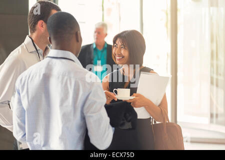 Imprenditrice a parlare con i colleghi holding tazza da caffè in ufficio Foto Stock