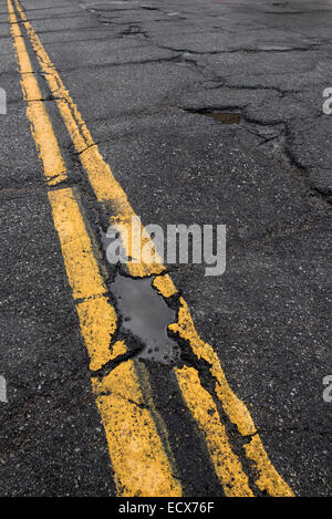 Buca e screpolata road con giallo linea di demarcazione in necessità di riparazione. Foto Stock