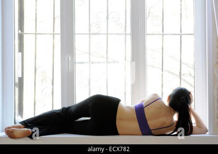 Donna con una coda di cavallo giacente su un davanzale appoggiata sul suo braccio Foto Stock