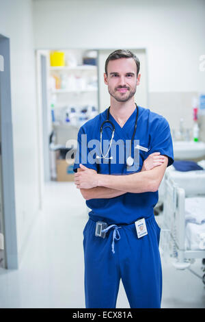 Ritratto di giovane maschio medico in piedi in ospedale con le braccia incrociate Foto Stock