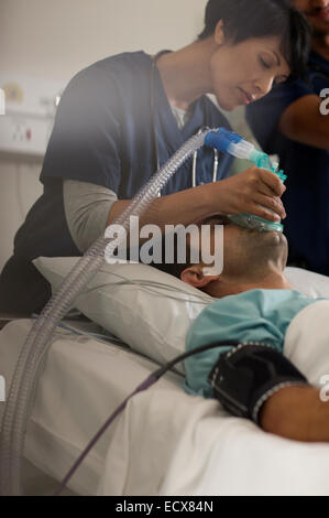 Medico tenendo le maschere di ossigeno su maschio della bocca del paziente in unità di terapia intensiva Foto Stock