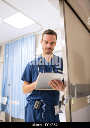 Medico maschio in piedi in porta, prendendo appunti su clip board in ospedale Foto Stock