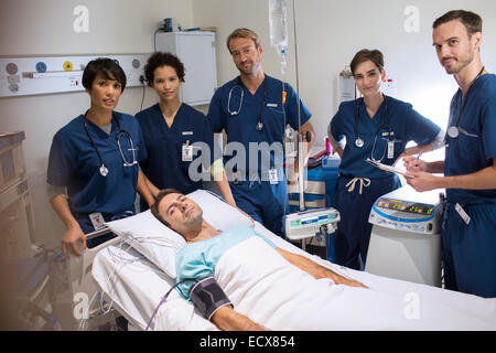 Team di medici in piedi intorno sorridente paziente sdraiato a letto in unità di terapia intensiva Foto Stock