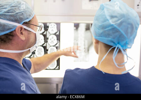 Vista posteriore dei chirurghi guardando del paziente x-ray e MRI scan in sala operatoria Foto Stock