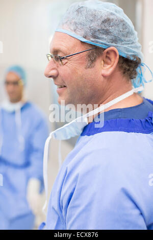 Vista laterale del chirurgo che indossano occhiali, blu cappuccio chirurgico e vestaglia Foto Stock