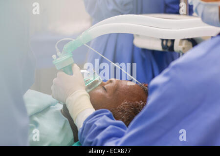 Close up medico indossando i guanti chirurgici, tenendo le maschere di ossigeno oltre il paziente in sala operatoria Foto Stock