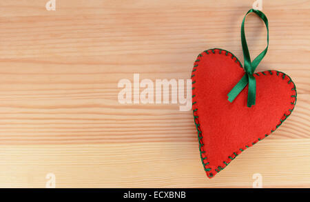 Rosso cucito a mano feltro decorazione di cuore con nastro verde su uno sfondo di legno con spazio di copia Foto Stock