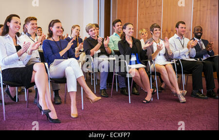 La gente di affari a guardare una presentazione in sala conferenze, battendo le mani e sorridente