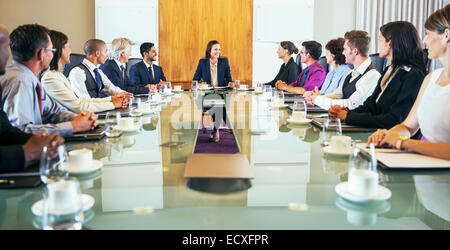 I partecipanti alla conferenza guardando alla giovane donna seduta a capo di un tavolo per conferenza Foto Stock