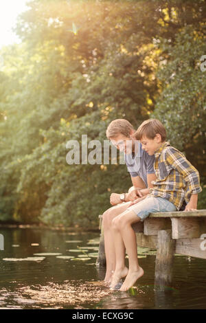 Padre e figlio piedi penzolanti nel lago Foto Stock