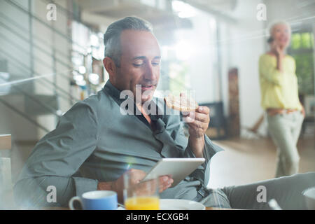 Uomo anziano con tavoletta digitale al tavolo per la colazione Foto Stock