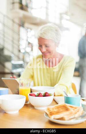 Donna anziana con tavoletta digitale al tavolo per la colazione Foto Stock