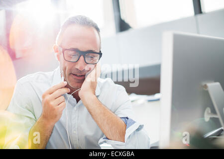 Imprenditore ascoltando gli auricolari alla scrivania in ufficio Foto Stock