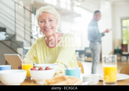 Donna anziana con tavoletta digitale al tavolo per la colazione Foto Stock