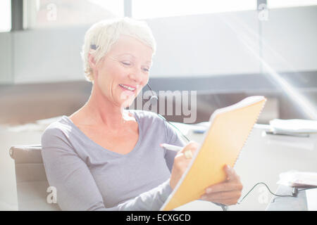 Imprenditrice in cuffia la scrittura sul blocco note in Office Foto Stock