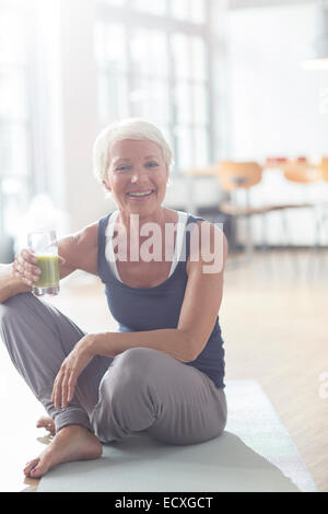 Donna anziana di bere succo di frutta sul tappeto di esercizio Foto Stock