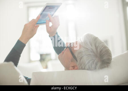 Uomo anziano con tavoletta digitale in salotto Foto Stock
