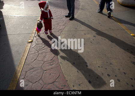 Tijuana, Messico. Xxi Dec, 2014. Una bambina vestito come Babbo Natale gioca con la sua bambola mentre i suoi genitori che prendono parte all'atletica gara di natale 'Esegui Santa Run, nella città di Tijuana, Baja California, nel nordovest del Messico il 21 dicembre 2014. Credito: Guillermo Arias/Xinhua/Alamy Live News Foto Stock