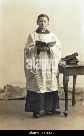 Cirillo per collezionisti. Giovane ragazzo adolescente coro da indossare accappatoio, in piedi, guardando il viewer 1910's bianco e nero fotografia colorata Foto Stock